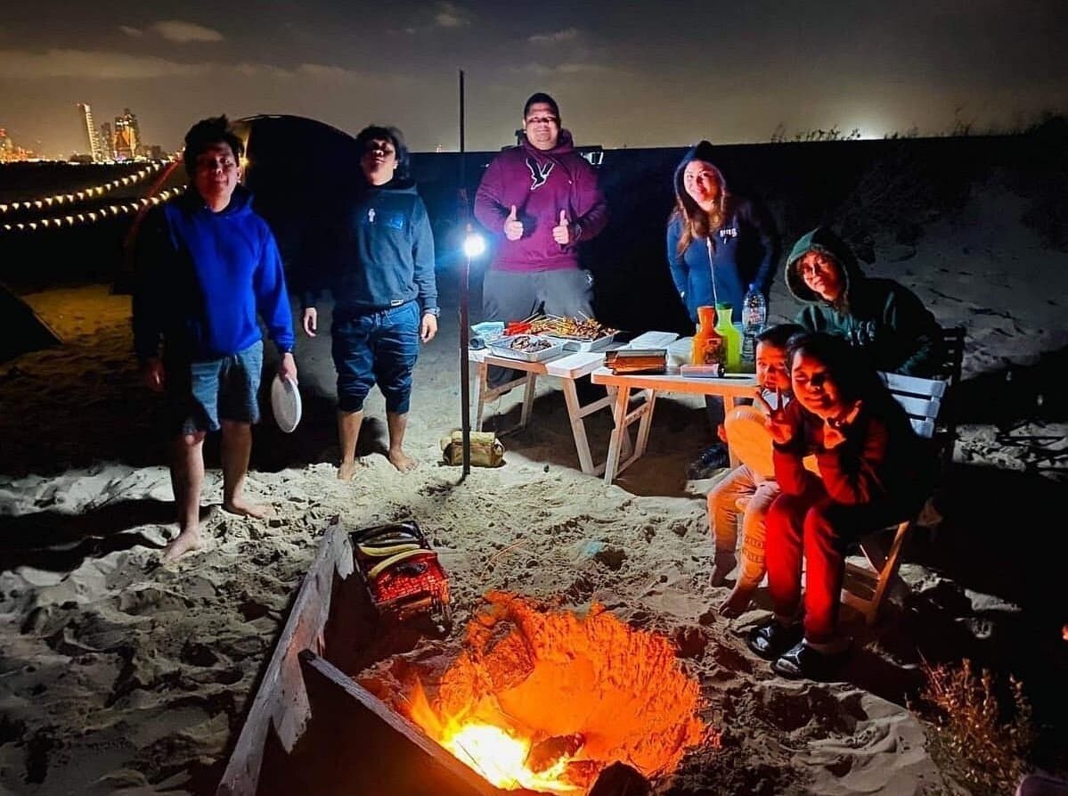 Group of friends around a campfire and BBQ table on the beach at night